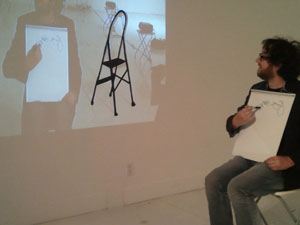 Michael Trigilio, who participated in the performance, draws a self-portrait while looking at a projected image of himself. 