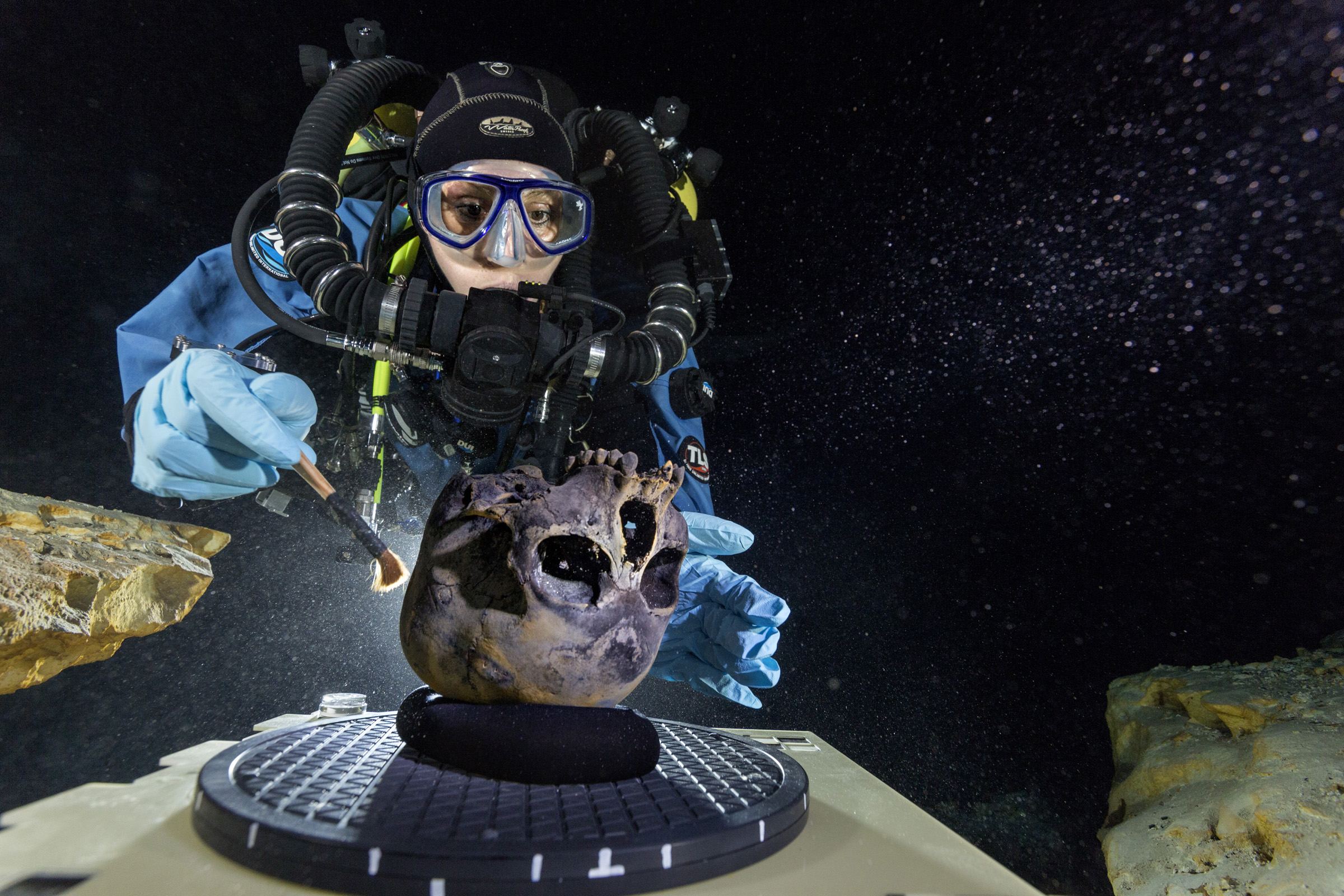 Diver Susan Bird working at the bottom of Hoyo Negro, a large dome-shaped underwater cave on Mexico’s Yucatán Peninsula. She carefully brushes the human skull found at the site while her team members take detailed photographs.