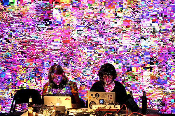 Two women sitting behind computer screens with colorful code displayed behind them